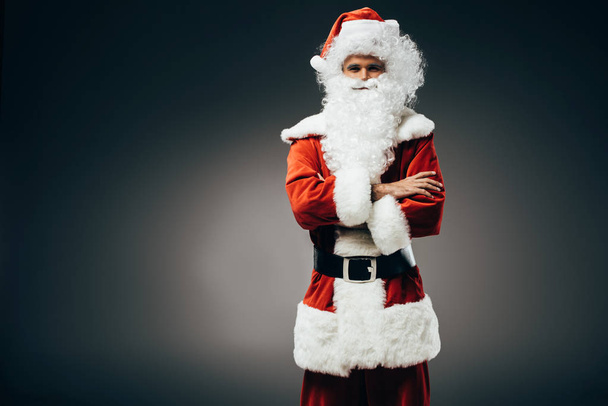 Άγιος Βασίλης σε κοστούμι στέκεται με σταυρωμένα χέρια απομονώνονται σε γκρι φόντο  - Φωτογραφία, εικόνα
