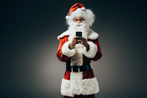 happy santa claus in costume using smartphone isolated on grey background  - Zdjęcie, obraz