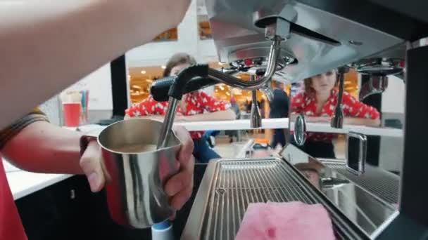 Barista chicoteia leite em uma máquina de café, cliente olhando para ele
 - Filmagem, Vídeo