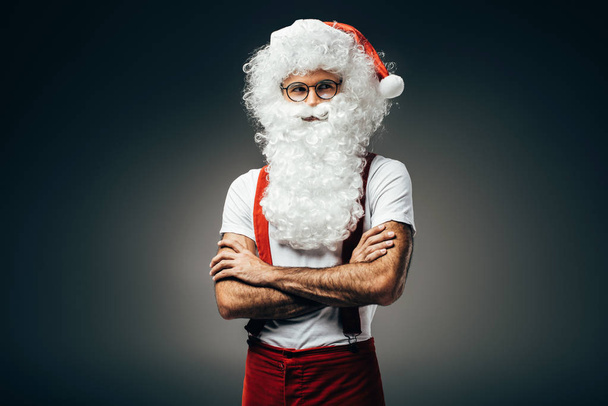 Papai Noel em óculos de pé com braços cruzados isolados sobre fundo cinza
  - Foto, Imagem