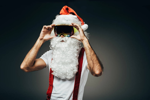 Santa claus adjsuting ski masker geïsoleerd op een grijze achtergrond  - Foto, afbeelding