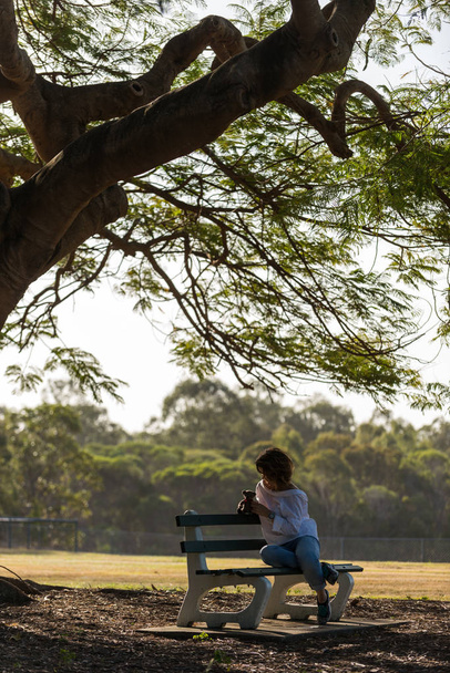 Girl sitting on a bench under a big tree - 写真・画像