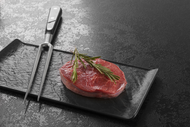 Luxus nyers friss marha steak és a hús villát a sötét háttéren fekete lemez. - Fotó, kép