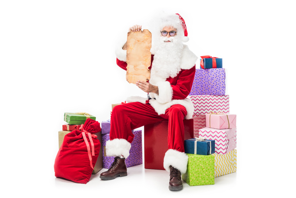 santa claus showing empty old parchment and sitting on pile of gift boxes isolated on white background  - Φωτογραφία, εικόνα