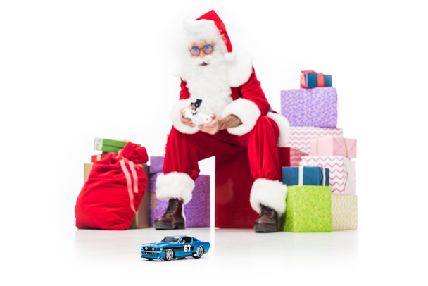 Babbo Natale seduto su mucchio di scatole regalo e utilizzando auto radiocomandata isolata su sfondo bianco
  - Foto, immagini
