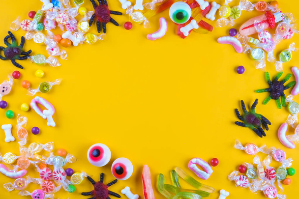 Assorted teeth & eyeball shaped candy spread on yellow background, jelly spider, gummy worms, sugar bones, round lollipop and other mixed candy, bloody finger. Top view, copy space, close up, flat lay - Foto, immagini