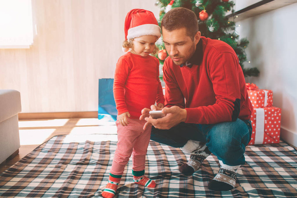 Merry Christmas and Happy New Year. Father and daughter stand together. Parent hold cellphone in hands. They both look at gadget. People are serious and concentrated. - Foto, imagen