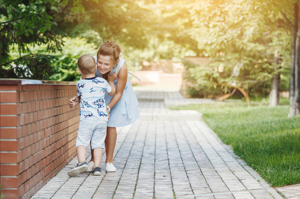 Young happy family: mother and blond boy walking on a stone pavement in the park. The concept of family well-being and a healthy lifestyle. - Photo, Image