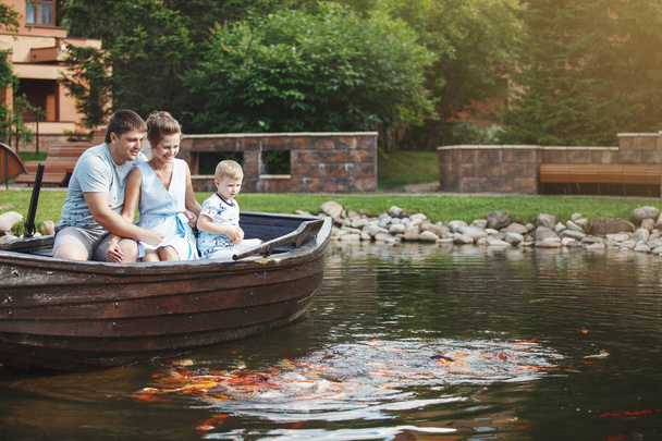 Moeder, vader en zoon zitten in een houten boot met roeispanen en voeden van de vissen met brood. - Foto, afbeelding
