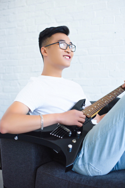 αποσυνδεθεί από χαρούμενος όμορφος Ασίας κιθαρίστας παίζει ηλεκτρική κιθάρα στο σπίτι - Φωτογραφία, εικόνα