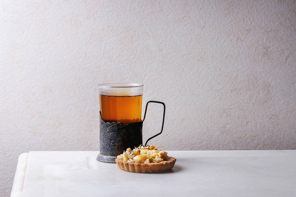 Σπιτικό γλυκό μηλόπιτα τάρτα κουλουράκι στο άσπρο πιάτο, ποτήρι ζεστό τσάι vintage ποτηροθήκη λευκό μαρμάρινο τραπέζι. Το φθινόπωρο το ψήσιμο. Μινιμαλιστικό στυλ. - Φωτογραφία, εικόνα