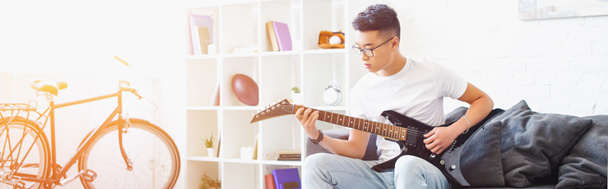 vista panorámica del hombre asiático guapo zurdo tocando la guitarra eléctrica en el sofá en casa
 - Foto, imagen