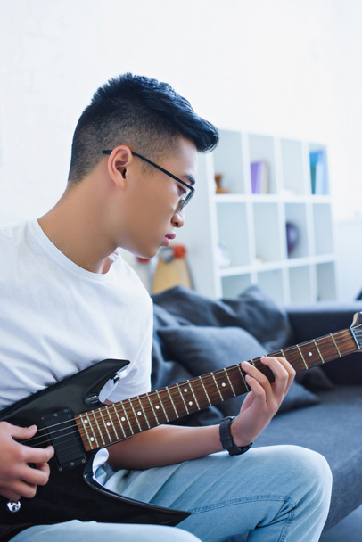 handsome asian man playing electric guitar at home - Foto, afbeelding