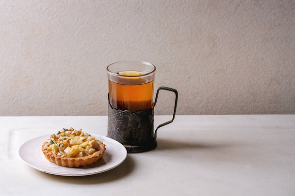 Σπιτικό γλυκό μηλόπιτα τάρτα κουλουράκι στο άσπρο πιάτο, ποτήρι ζεστό τσάι vintage ποτηροθήκη λευκό μαρμάρινο τραπέζι. Το φθινόπωρο το ψήσιμο. Μινιμαλιστικό στυλ. - Φωτογραφία, εικόνα