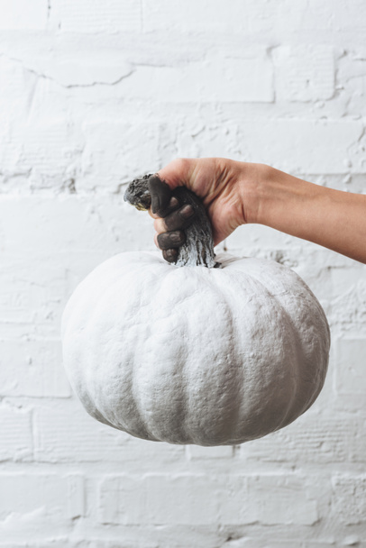 cropped shot of woman holding white painted halloween pumpkin in front of white brick wall - Foto, Imagen