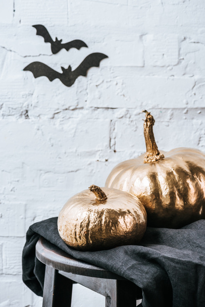 halloweenclose-up shot of two halloween pumpkins painted in golden metallic in front of white brick wall with bat stickers - Fotó, kép