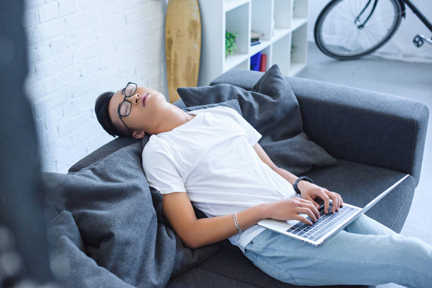 hoge hoekmening van jonge Aziatische man slapen en laptop op de Bank thuis te houden - Foto, afbeelding