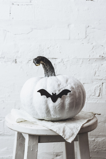close-up shot of white painted halloween pumpkin with bat sticker in front of white brick wall - Fotografie, Obrázek