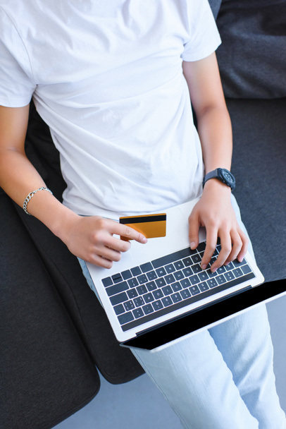 körülvágott kép az ember használ laptop és hitelkártya gazdaságot kanapé otthon - Fotó, kép