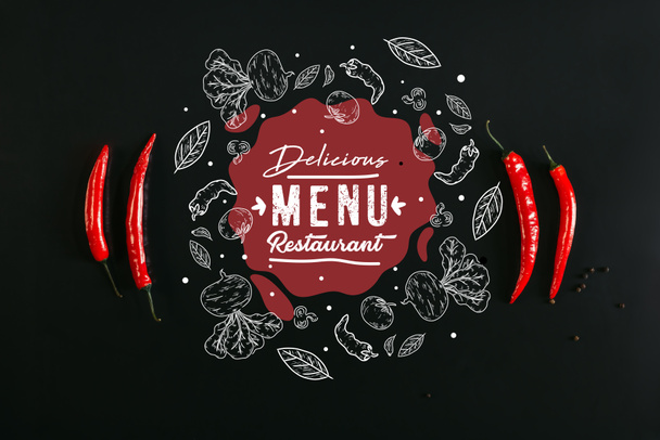 top view of red chili peppers and peppercorns on black background with "delicious menu restaurant" lettering  - Valokuva, kuva
