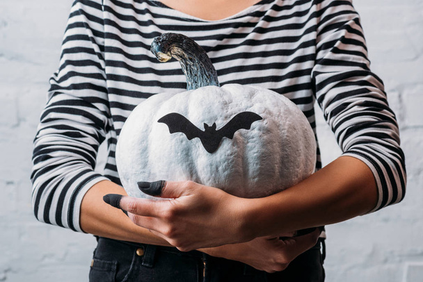 cropped shot of woman holding white painted halloween pumpkin with bat sticker - Foto, Bild