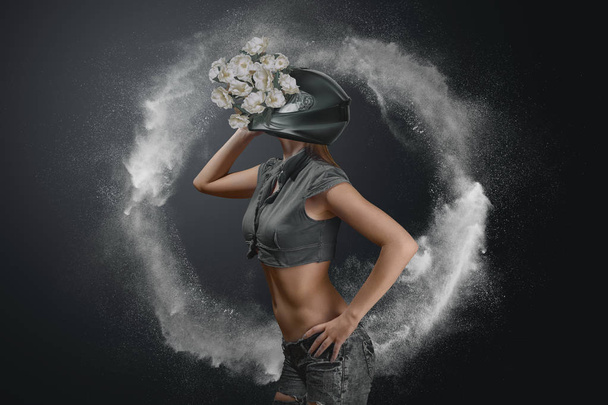 Concept abstract fashion portrait of young woman in motorcycle helmet with flowers - 写真・画像