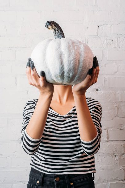 woman in striped shirt holding white painted halloween pumpkin in front of head - Foto, Imagen