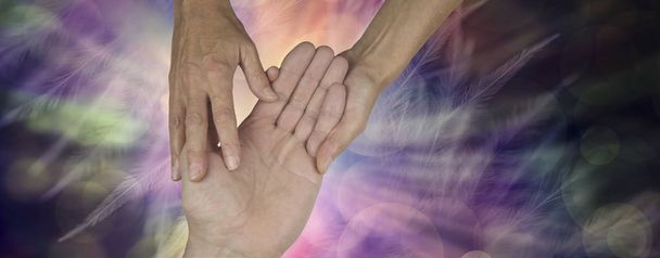 Palmistry Website Banner - weibliche Hände halten und erforschen männliche offene Hand vor einem ätherischen Federeffekt mehrfarbigem Hintergrund mit Kopierraum - Foto, Bild