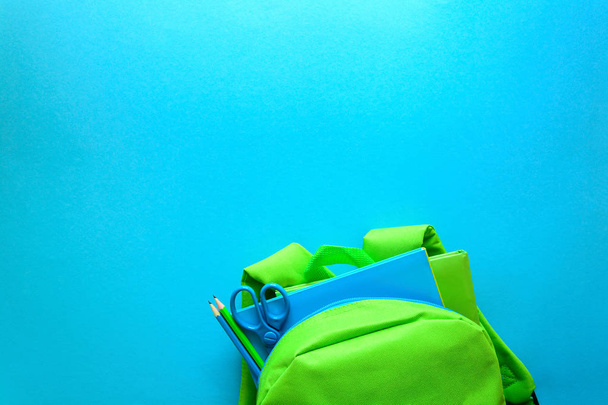 Back to school concept. Green backpack with school supplies on blue background. Top view. Copy space - Фото, зображення