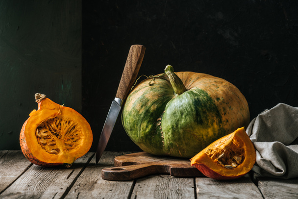 close up view of food composition with pumpkins, knife and cutting board on wooden surface on dark background - Photo, Image