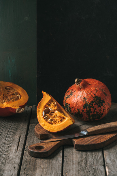 close up view of raw cut pumpkins arranged on cutting board with knife on dark backdrop - 写真・画像