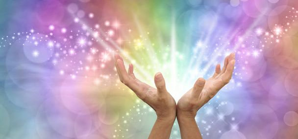 Senden von wunderschöner, kraftvoller, weißer Licht-Heilungsenergie - Paar offene Hände mit weißer Energie, die nach außen vor einem funkelnden, regenbogenfarbenen Hintergrund strahlen - Foto, Bild