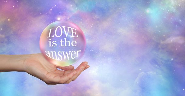 Whatever your Question LOVE is the answer - large transparent ball floating above an open palm containing the words LOVE IS THE ANSWER on a heavenly celestial sky background with copy space - Photo, Image