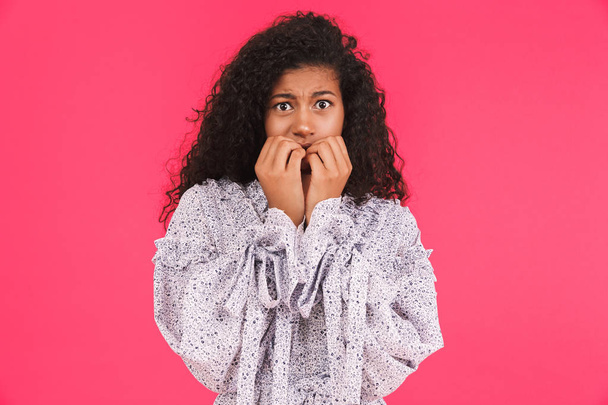 Portrait of a scared young african woman in summer dress standing isolated over pink background, cover mouth - Valokuva, kuva