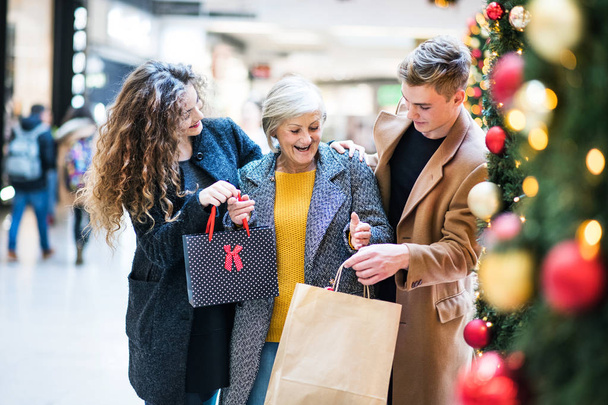 A portrait of grandmother and teenage grandchildren in shopping center at Christmas. - Fotografie, Obrázek