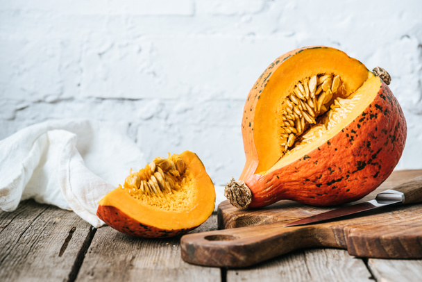 close up view of cut pumpkin on cutting board on wooden surface and white brick wall background - Photo, Image