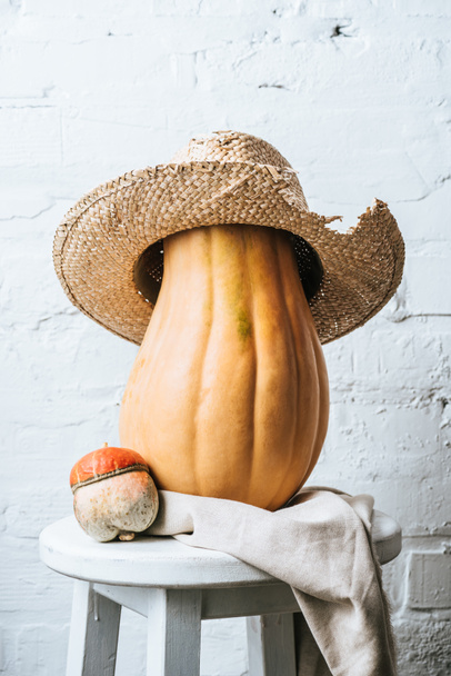 close up view of pumpkins and straw hat on wooden chair with linen on white brick wall background - Foto, immagini