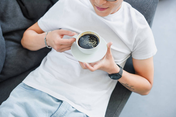 ソファで休んでいる間一杯のコーヒーを保持している若い男のクロップ撮影 - 写真・画像