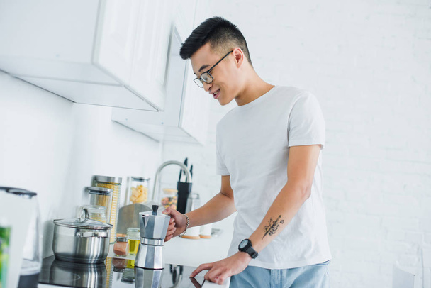 komea hymyilevä nuori aasialainen mies keittää kahvia keittiössä
 - Valokuva, kuva