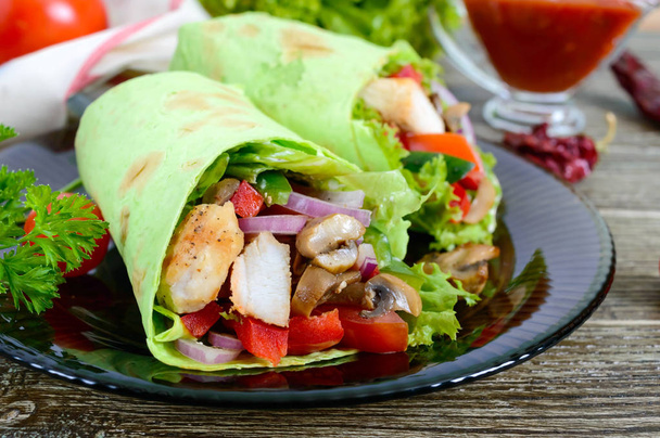 Burrito mit Huhn, Gemüse, Pilzen im Fladenbrot mit Spinat auf einem Holztisch. Mexikanisches Essen. - Foto, Bild