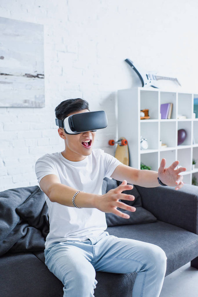 young man sitting on couch and using virtual reality headset at home  - 写真・画像