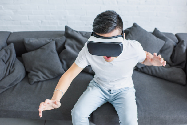 hoge hoekmening van emotionele jonge man zittend op de Bank en met behulp van virtual reality headset - Foto, afbeelding