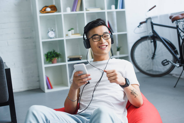 smiling young man using smartphone and listening music in headphones  - Zdjęcie, obraz