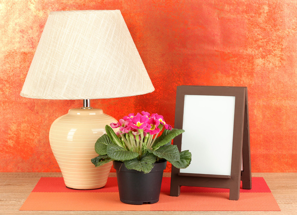 Brown photo frame and lamp on wooden table on red wall background - Zdjęcie, obraz