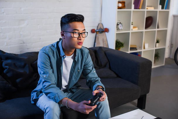 jonge Aziatische man afspelen van video game met joystick thuis gericht  - Foto, afbeelding