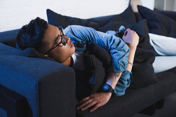 молодой азиат в очках спит дома на диване
  - Фото, изображение