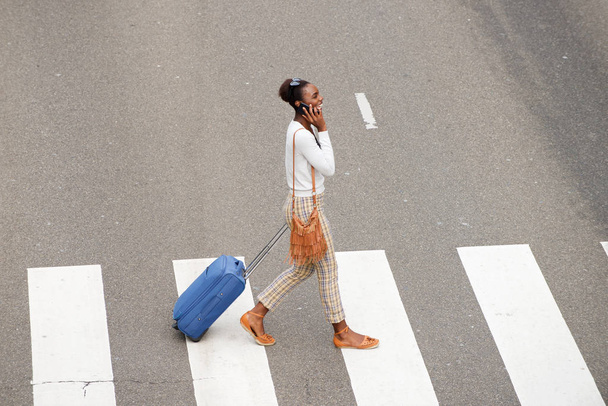 Volledige lichaam kant portret van Afro-Amerikaanse vrouw oversteken van de straat met Sporttassen en mobiel - Foto, afbeelding