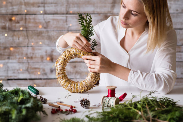 A young woman making a Christmas wreath. - Fotó, kép