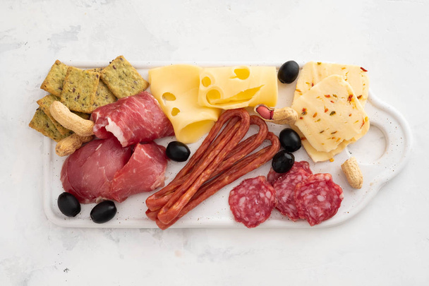 Cured meat platter of traditional Spanish tapas - chorizo, salsichon, jamon serrano, lomo - erved on white board with olives. - Foto, afbeelding