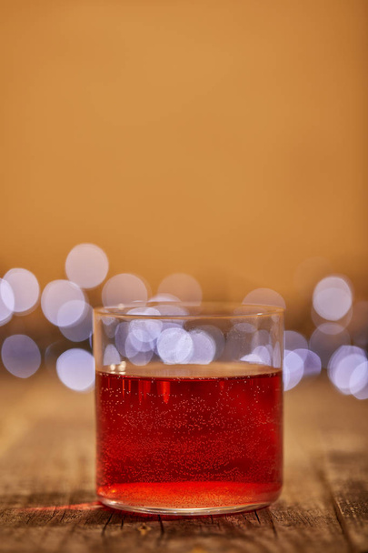close up view of tasty mulled wine in glass on wooden surface with defocused bokeh lights on backdrop - Foto, afbeelding